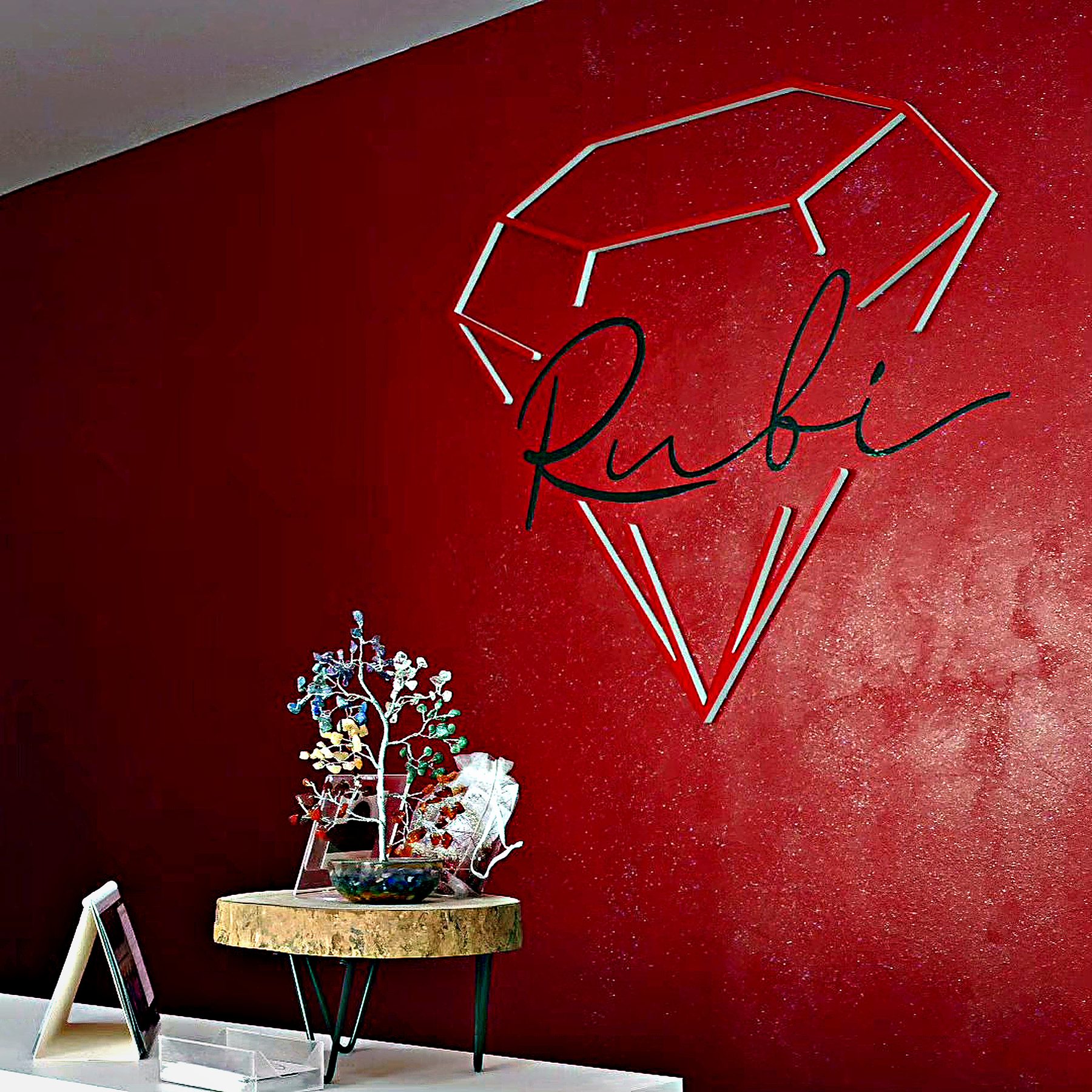Pared roja de Centros Rubí con el diamante de neón y la firma «Rubí», junto a una mesa auxiliar con una escultura floral